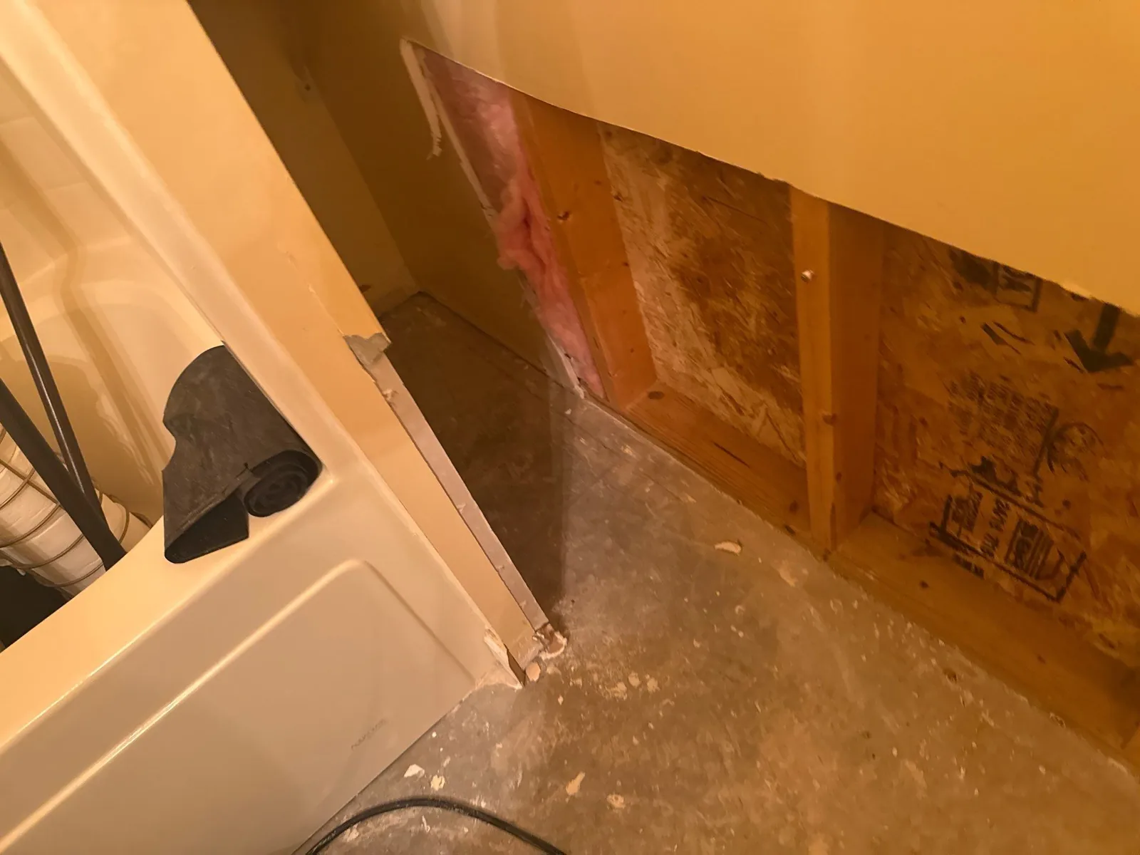 Bathroom showing mid-phase water mitigation with exposed wall and insulation, indicating water damage. Bathtub corner and rolled material visible — serving Dallas, GA.