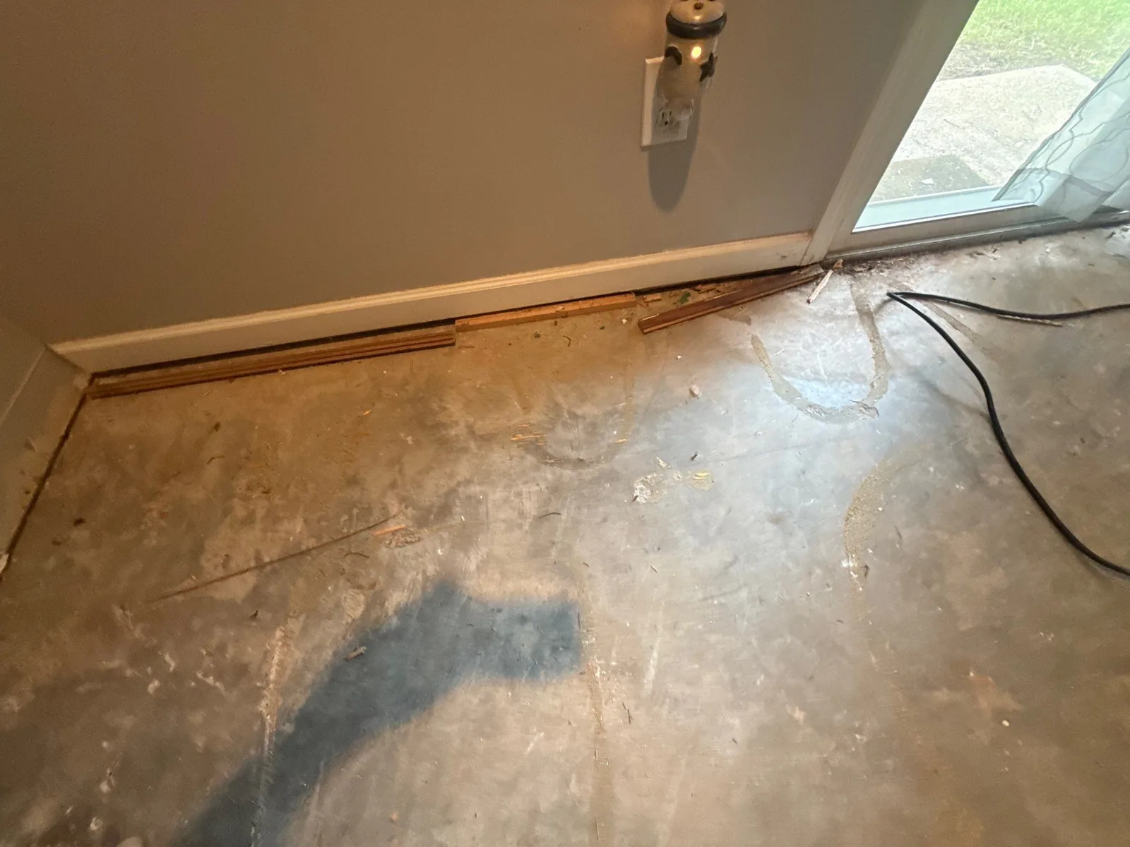 Room with cement floor and wooden trim during construction phase. Near wall with electrical outlet and glass door — serving Dallas, GA.