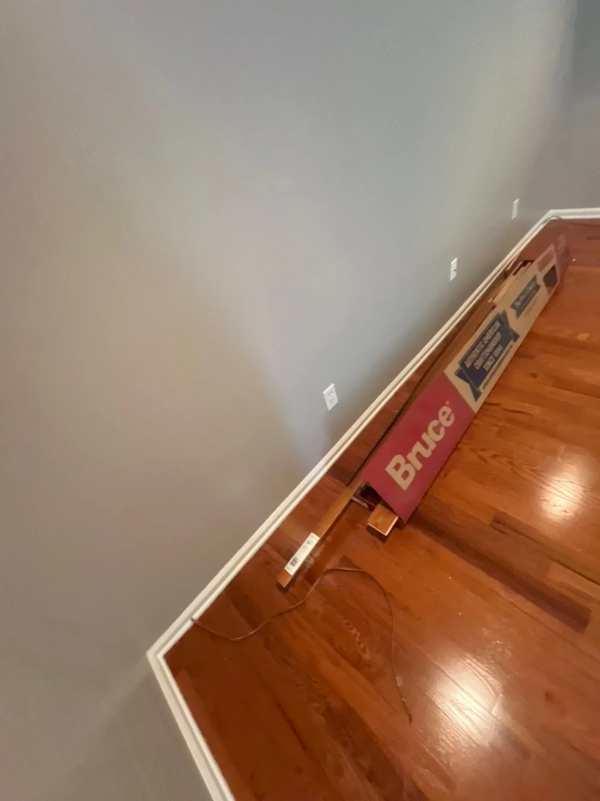 Room with gray walls and new hardwood flooring, box labeled 'Bruce' on the floor with additional materials — serving Dallas, GA.