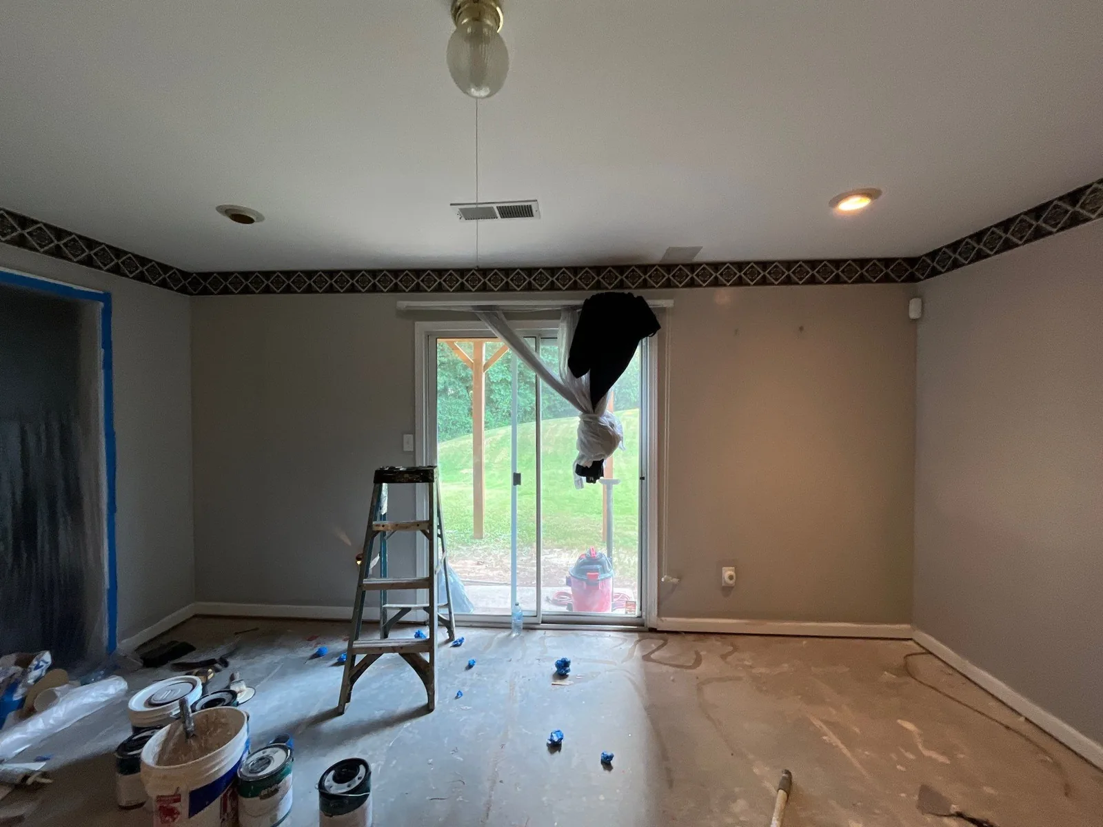 Room under renovation with paint cans, a ladder, and covered windows. Floor partly covered and paint supplies scattered — serving Dallas, GA.