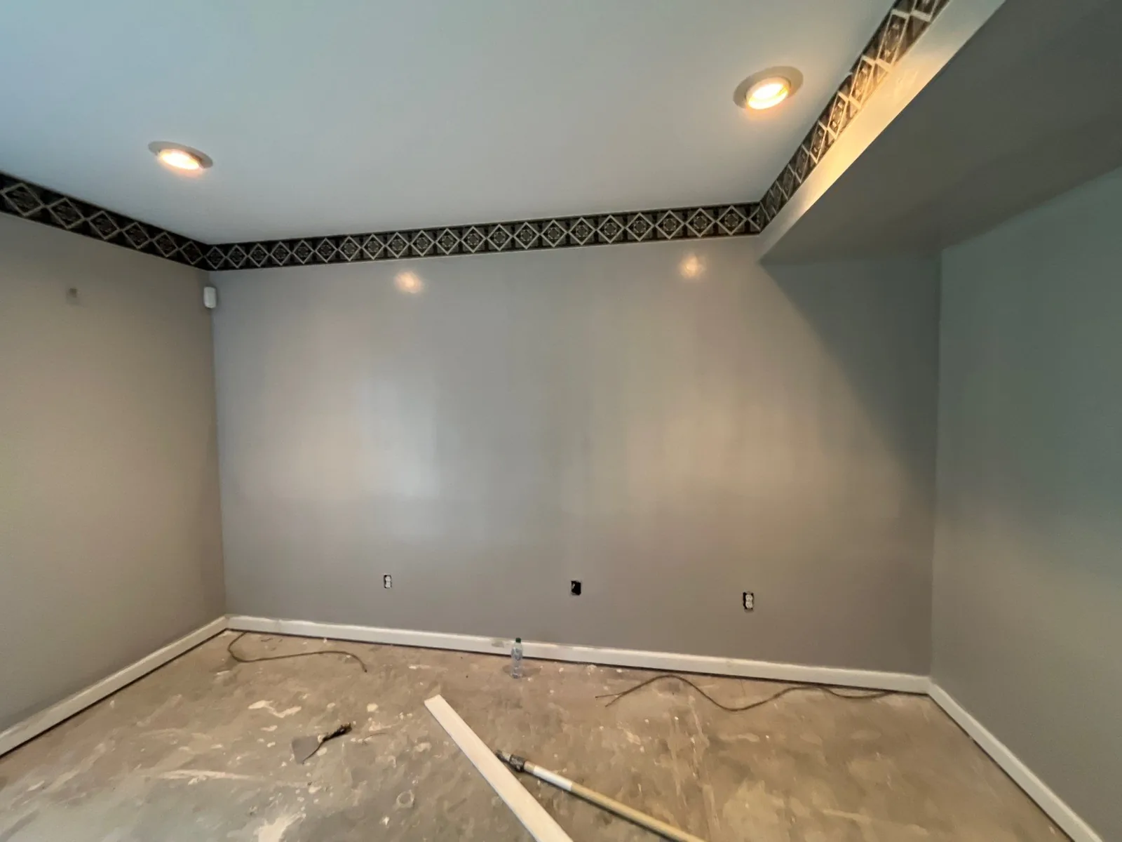 Room under renovation with gray walls, recessed lighting, decorative border trim, and unfinished flooring — serving Dallas, GA.