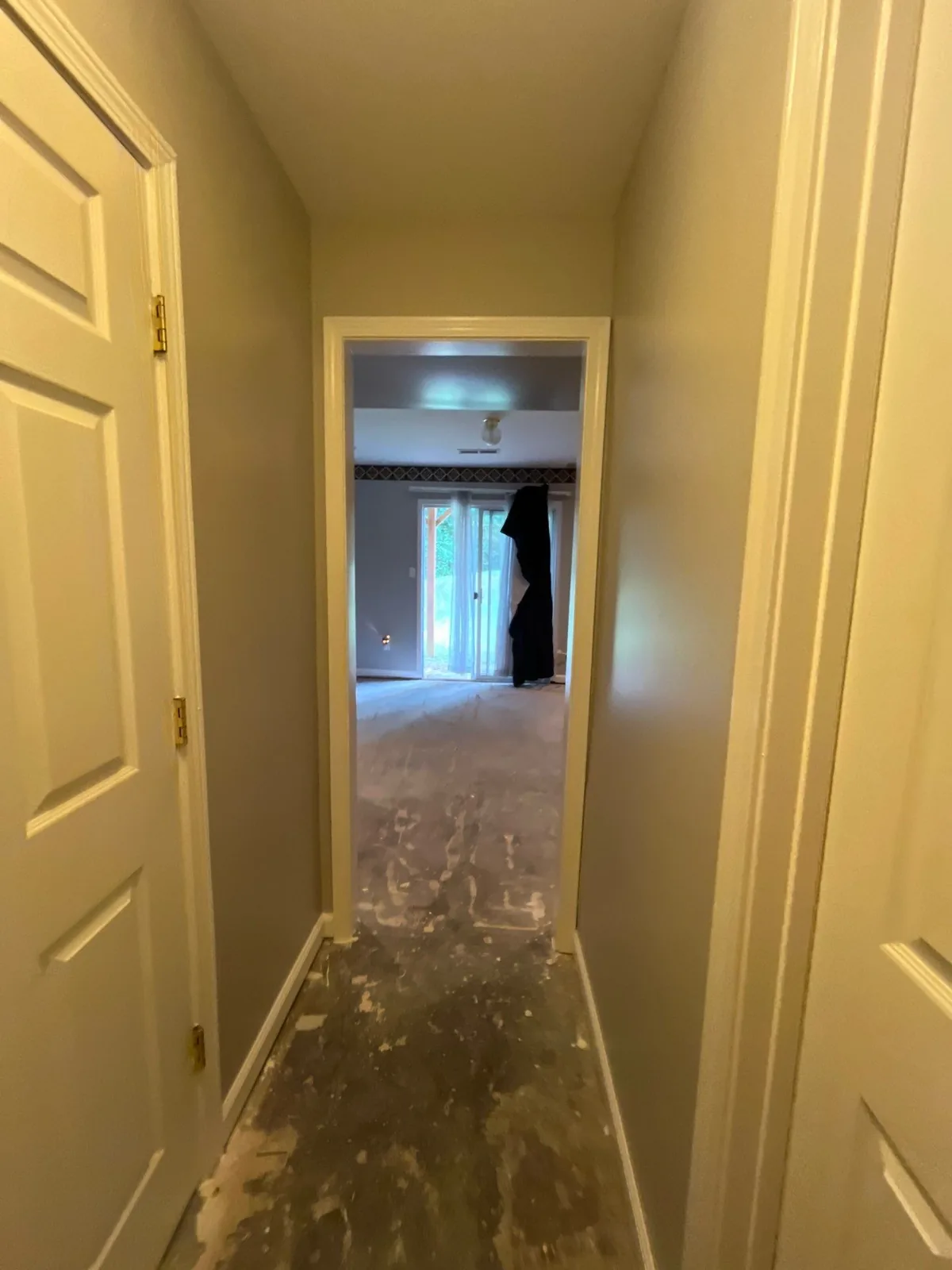 View down a hallway with a partially covered floor towards a room with open doors and a backyard view — serving Dallas, GA.