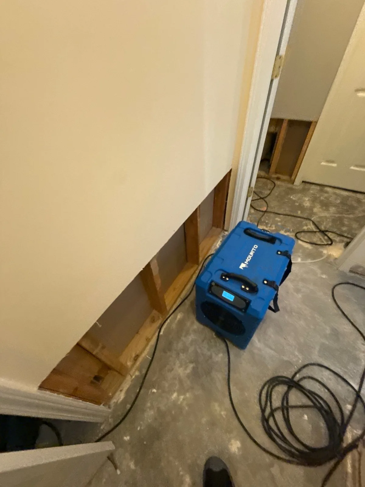 Interior view of a room with a partially removed wall, exposing wooden framing. A blue drying machine is on the floor, indicating water mitigation work — serving Dallas, GA.