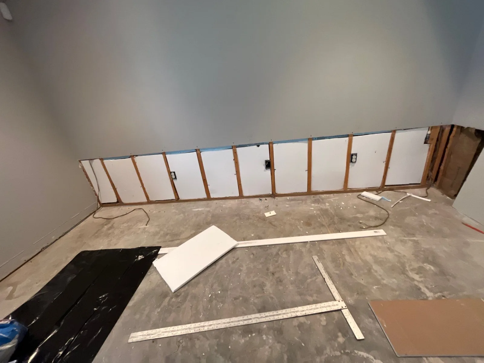 Partial wall demolition with exposed studs and electrical outlets, materials and tools on the floor — serving Dallas, GA.