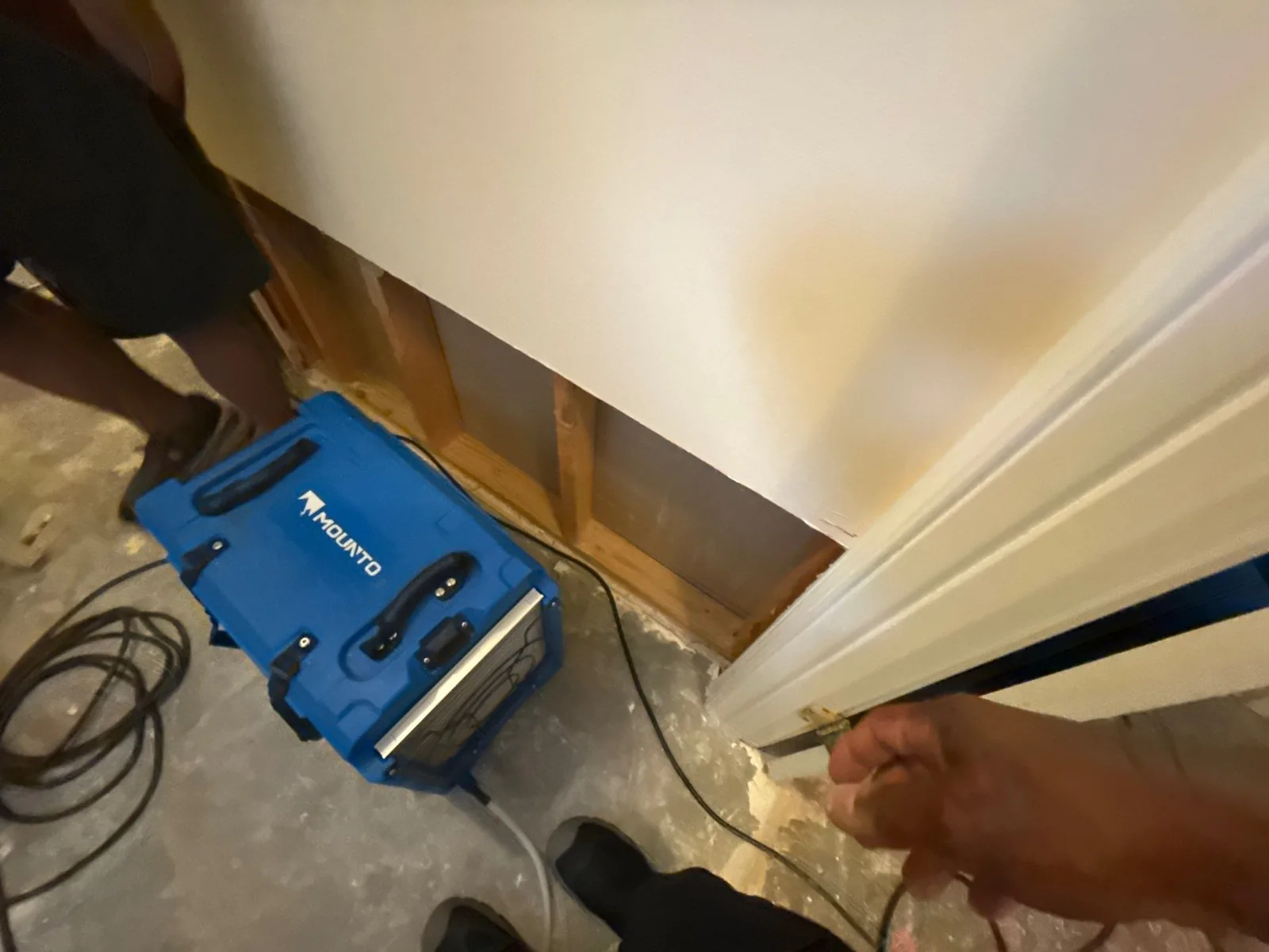 Interior scene with an exposed wall section and a blue dehumidifier on the floor during water mitigation — serving Dallas, GA.