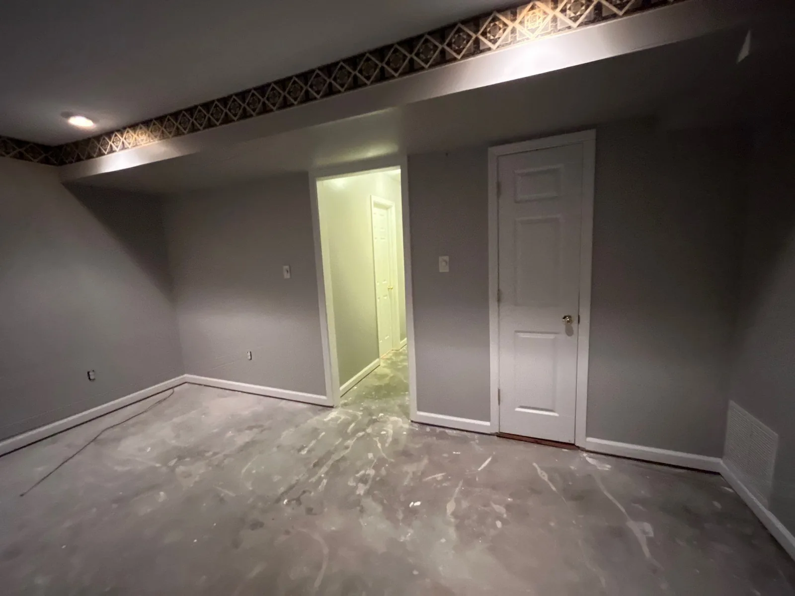 Room under construction with unfinished floors, newly painted walls, and a doorway to another area — serving Dallas, GA.