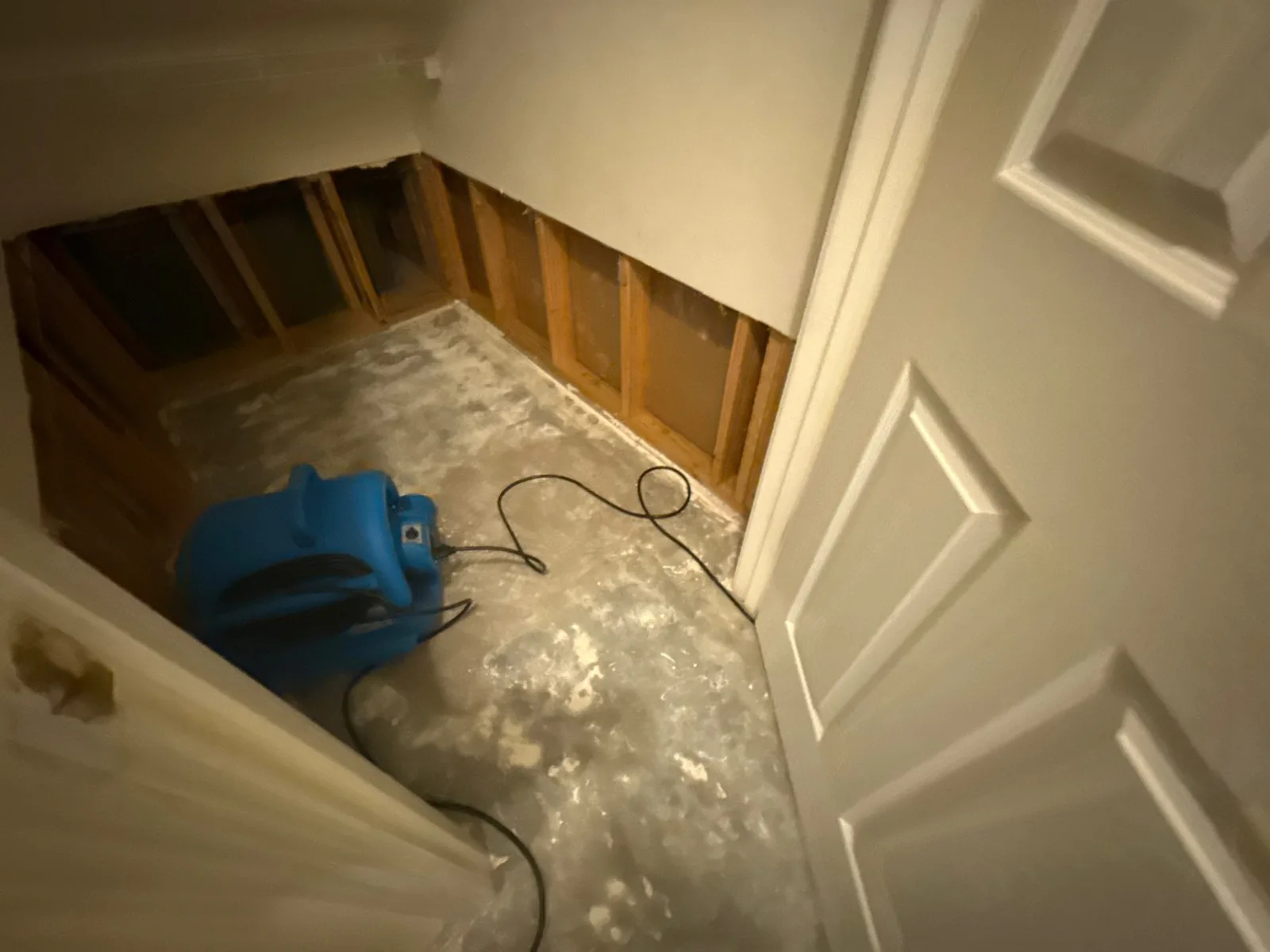 A room with exposed wooden studs in the wall, concrete floor, and a blue air mover, indicating water mitigation work — serving Dallas, GA.