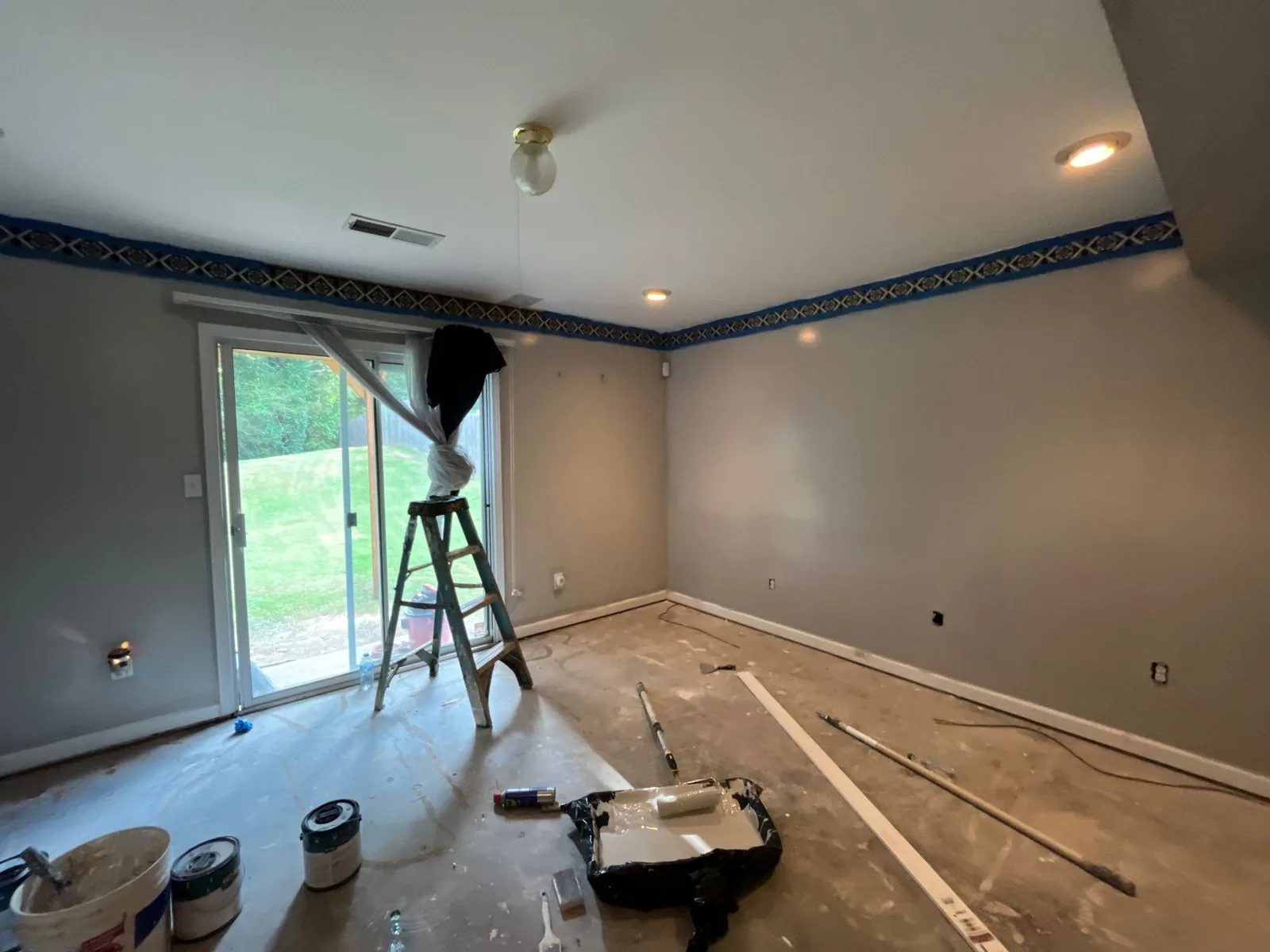 Room under remodeling with stepladder near window, painted walls, and painting supplies on the floor — serving Dallas, GA.