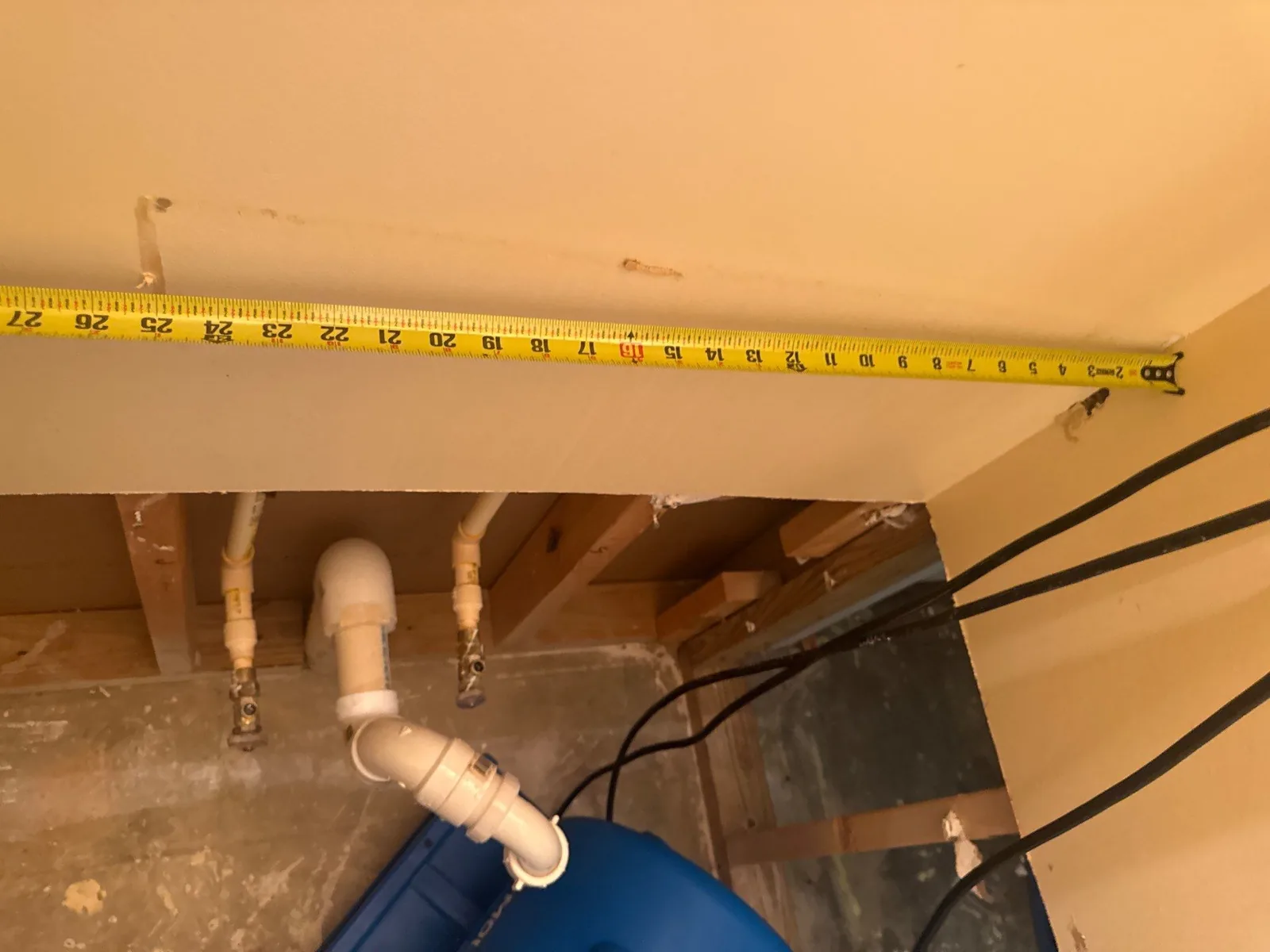 Measuring tape across a wall, exposed plumbing and blue dehumidifier visible during water mitigation work — serving Dallas, GA.