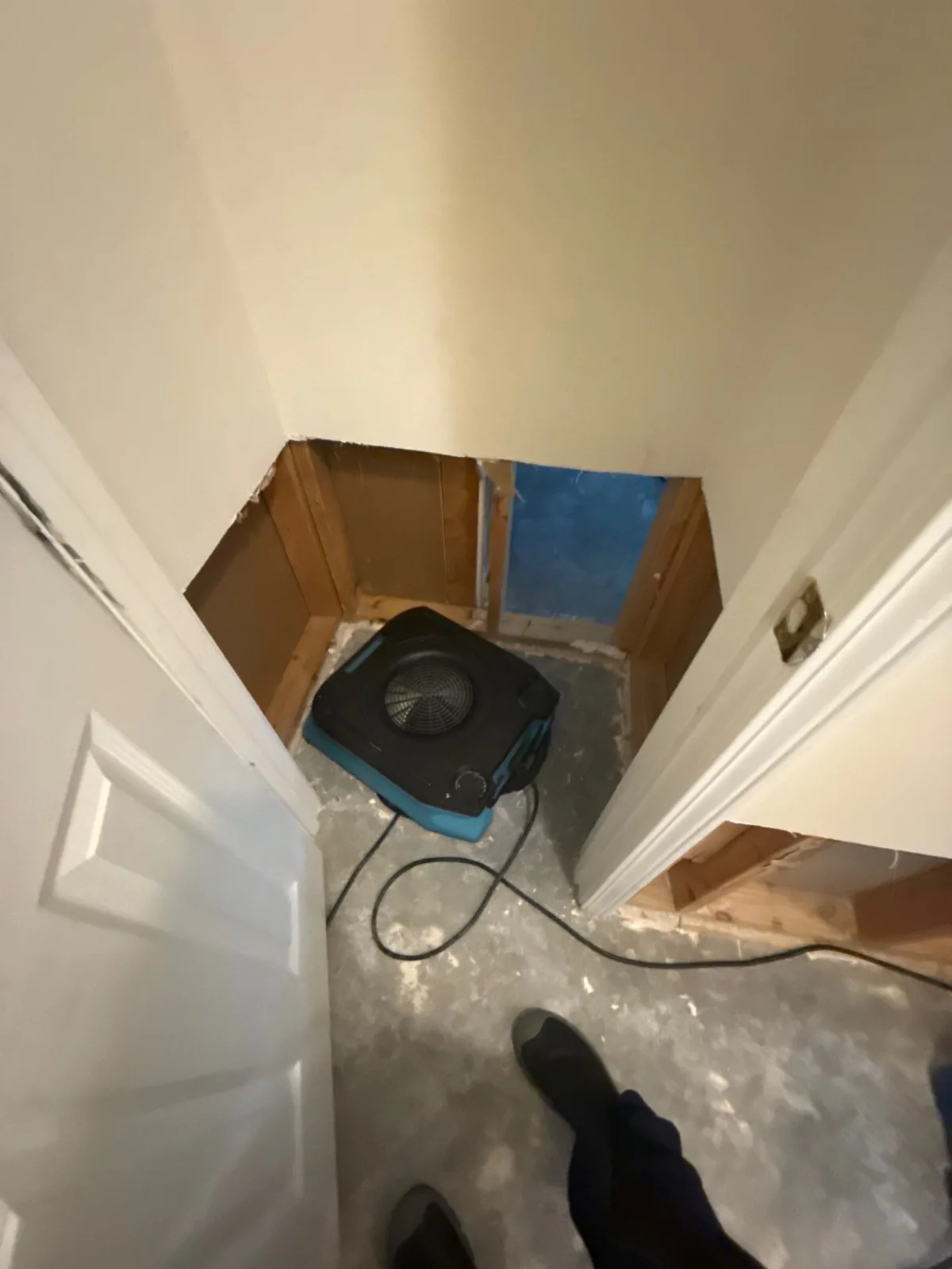 Room with drywall removed exposing studs and blue moisture barrier, with an air mover on the floor — serving Dallas, GA.
