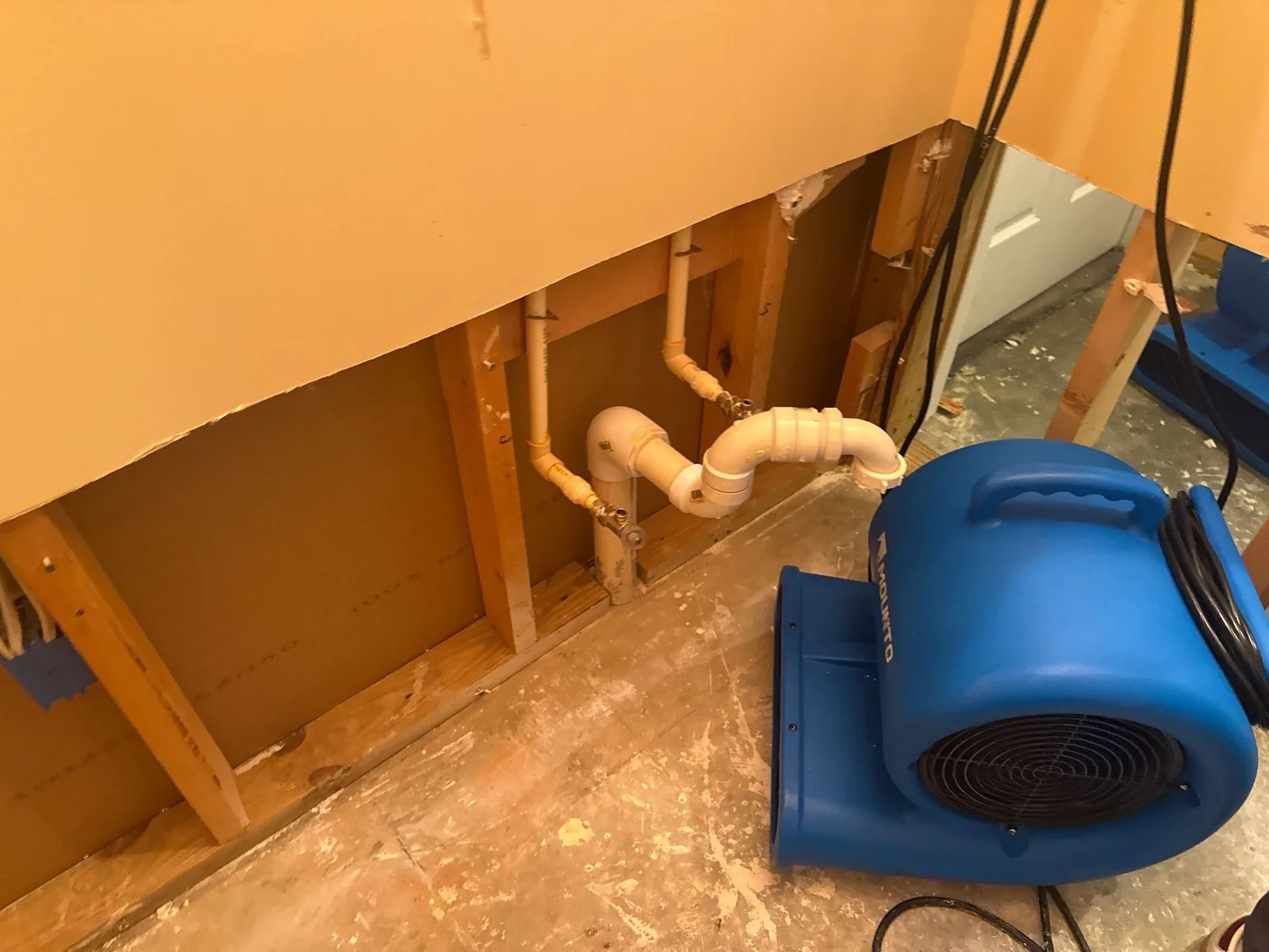Interior wall with exposed plumbing and a blue air mover for water mitigation — serving Dallas, GA.
