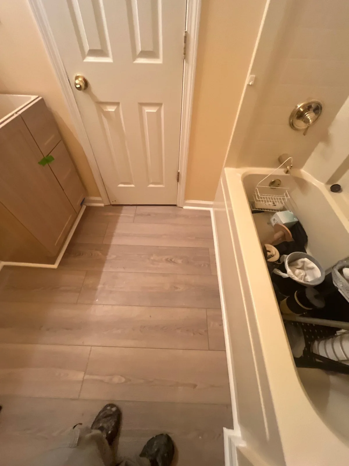 Bathroom with new flooring, a wooden cabinet, closed door, and a bathtub containing personal items and toiletries — serving Dallas, GA.