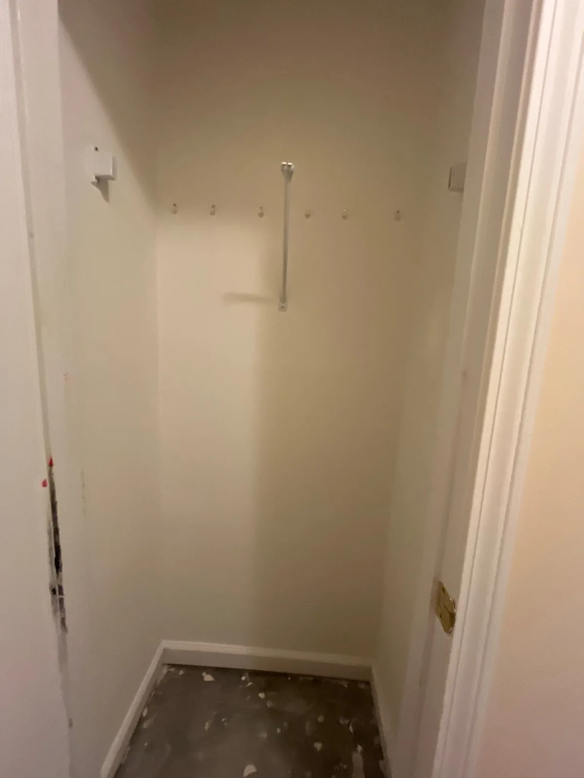 Empty closet under construction with hooks and a metal rod installed, unfinished floor with plaster — serving Dallas, GA.