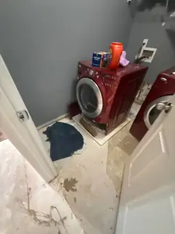 Laundry room floor peeling and saturated during water damage assessment beside red front-load washer and dryer — Smyrna, GA
