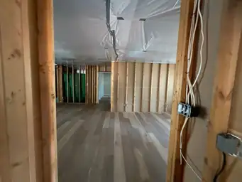 Room during storm damage assessment with stripped wall studs, poly ceiling barrier, and new light oak flooring installed — Kennesaw, GA