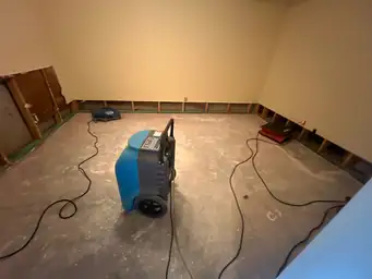 Large blue dehumidifier and air movers on bare concrete basement floor with cut-out lower drywall perimeter during drying phase — Marietta, GA