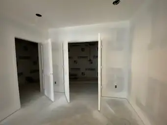 Basement bedroom showing painted drywall with two open white doors revealing unfinished storage space behind walls — Metro Atlanta, GA