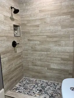 Basement bathroom walk-in shower with wood-look porcelain tile walls and pebble stone accent column — Atlanta, GA