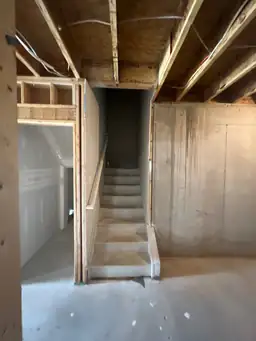 Basement staircase rough-in with concrete foundation walls, exposed OSB ceiling joists, and partial drywall panel — Metro Atlanta, GA