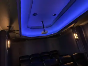 Basement home theater projector mounted above glowing blue LED stage platform with wall sconce lighting — Atlanta, GA