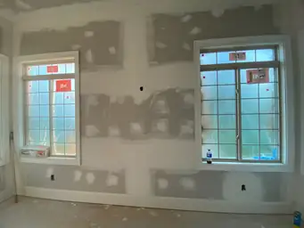 Sunroom drywall walls with compound patches flanking two multi-pane windows and center partition during flooring phase — Marietta, GA