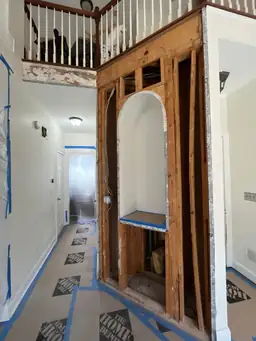 Kitchen demo phase — wall framing exposed for new arched opening construction, staircase and balcony visible, floors protected — Powder Springs, GA