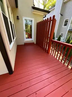 Side-angle view showing new red-coated deck boards next to original unpainted railing during deck stain comparison — Marietta, GA