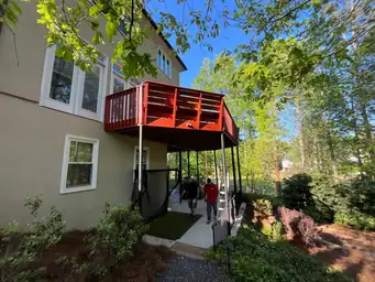Deck repair contractor crew working below completed red-stained elevated deck structure beside two-story home — Marietta, GA