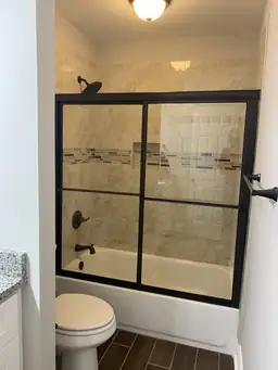 Bathroom remodel with travertine tile shower walls, mosaic accent strip, and frameless black-grid glass door — Metro Atlanta, GA