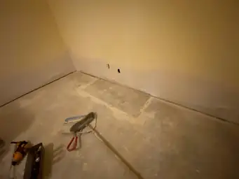 Gray drywall corner finished with joint compound and roller tool, bare concrete slab floor visible during basement reconstruction — Marietta, GA