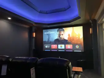 Basement home theater with large projector screen, blue LED stage platform, and tiered leather recliner rows — Atlanta, GA