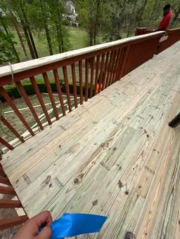 Contractor taping off deck boards preparing new pressure-treated wood surface before deck staining begins — Marietta, GA