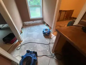 Two blue air movers and dehumidifier running in water-damaged basement with cut drywall, exposed studs, and bare subfloor — Marietta, GA