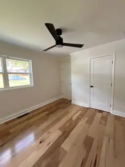 Completed bedroom after home remodel with light natural hickory hardwood floors, black ceiling fan, and white closet doors — Marietta, GA