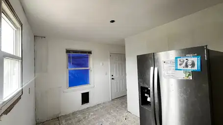 Storm-damaged kitchen with blue tarp over exterior window opening, stripped wall panels, and refrigerator in place — Acworth, GA