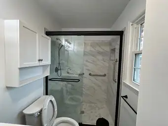 Completed bathroom after storm restoration with white marble-tile shower, black-framed glass door, and white vanity cabinet — Marietta, GA