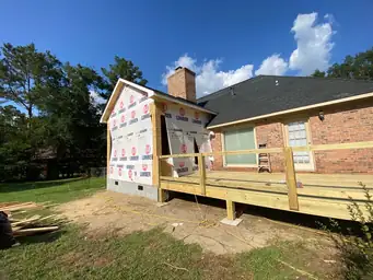 Sunroom addition wood stud framing walls with roof rafters and completed deck framing during insulation installation phase — Marietta, GA
