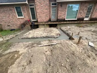 Worker leveling fresh concrete footing beside brick home during early ground-up home addition construction phase — Marietta, GA