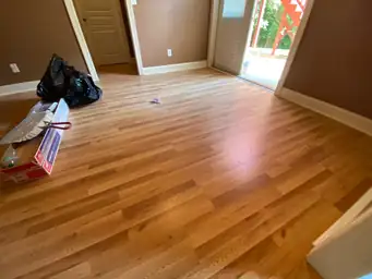 Basement room with warm brown walls and new oak hardwood flooring mid-installation, debris bags near open patio door — Marietta, GA