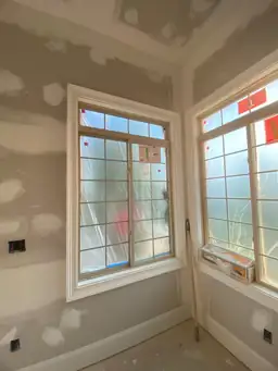 Two large multi-pane windows with white trim freshly set in drywall walls during sunroom addition with film protection — Marietta, GA