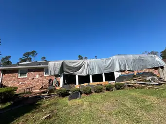 Brick home exterior after storm with large grey tarp across entire roof section and debris on lawn — Marietta, GA
