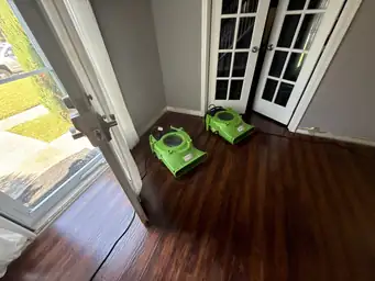 Completed water damage restoration showing refinished dark cherry hardwood floors and large bay window room — Smyrna, GA