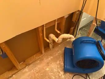 Interior wall with exposed plumbing and a blue air mover for water mitigation — serving Dallas, GA.