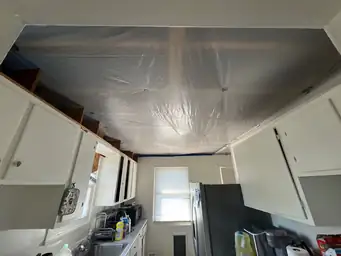 Kitchen ceiling with polyethylene containment sheeting over water-damaged cavity exposing structural framing above cabinets — Acworth, GA