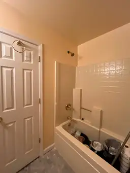 Bathroom under remodeling with bathtub filled with cleaning supplies and showerhead. Tiled walls and closed door with towel ring visible — serving Dallas, GA.