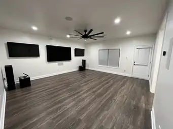 Open living renovation with dark wood plank ceiling, triple wall-mounted TVs, and surround-sound speaker system — Metro Atlanta, GA