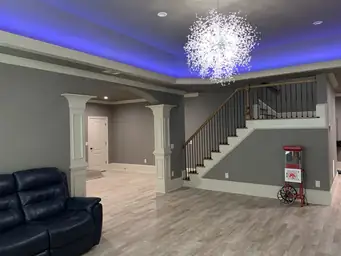 Finished basement with crystal chandelier, blue LED tray ceiling, white archway columns, and LVP flooring — Atlanta, GA