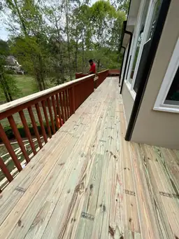 Worker applying stain to freshly installed pressure-treated boards along long second-story deck during deck repair — Marietta, GA