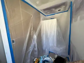 Bathroom interior wrapped in plastic sheeting and blue painter tape during spray painting phase of home remodel — Marietta, GA