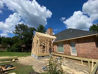 Sunroom addition exterior mid-construction with house wrap, framed wood deck structure, and pressure-treated stair stringers — Marietta, GA